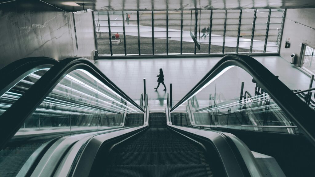 People using the sleek modern escalator in an indoor building with glass panels.