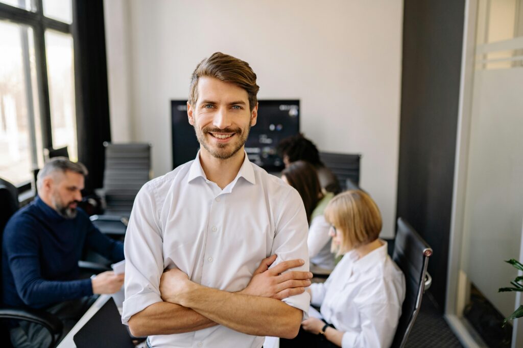 Smiling businessman standing confidently with arms crossed in an office setting.